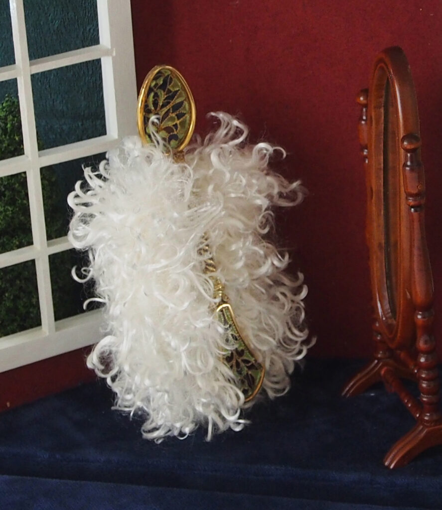 A lavish fur muff in white sits beside a small wooden vanity mirror, creating a vintage-inspired scene against a burgundy backdrop.